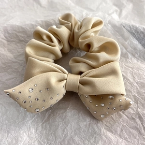 Detail of beige satin scrunchie with sparkling rhinestone bow on white paper
