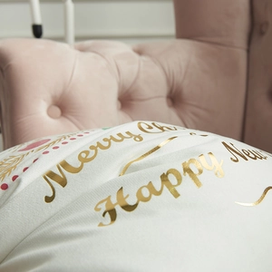 White Christmas pillow cover with gold foil lettering on a soft pink sofa