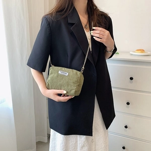Detail of olive green corduroy bag with golden chain strap worn by a model