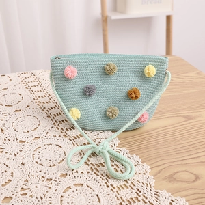 Detail of light mint green straw crossbody bag with colorful pom poms and bow strap