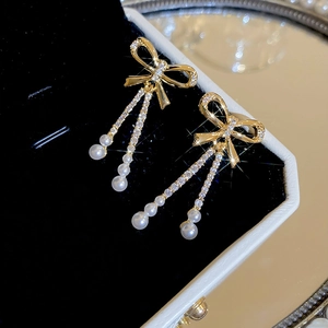 Macro view of gold bow earrings with shimmering zircon chains and small white pearls