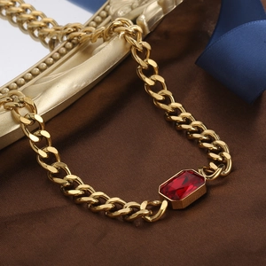 Detail van gouden Cubaanse ketting met rechthoekige rode kristallen hanger op zijden stof