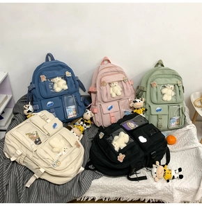 Cinque zaini scolastici minimalisti con ciondoli di peluche in un ambiente interno