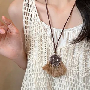 Macro detail of bohemian round engraved bronze pendant with light khaki cotton tassels