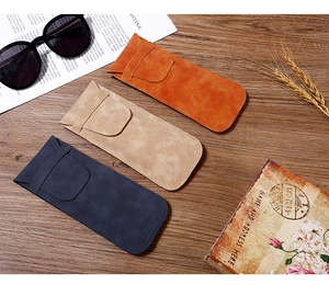 Tre custodie per occhiali in finta pelle scamosciata arancione, beige e blu su legno
