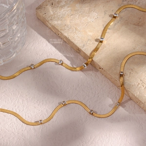 Detail of a golden herringbone chain necklace with inlaid cubic zirconia on marble base