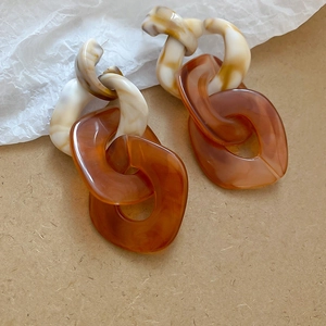 Macro shot of chunky resin chain earrings in amber and cream faux tortoise tones