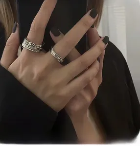 Detailed view of silver rings with irregular lava texture worn on hand with black nails