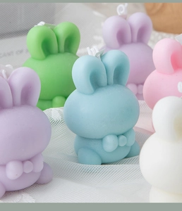 Close-up of cute rabbit-shaped candles in soft pastel colors on white mesh fabric background