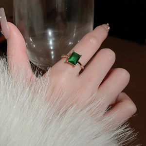 Detail of emerald green rectangular gemstone ring in rose gold on a model's hand