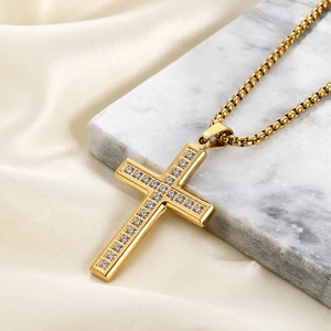 Polished gold cross pendant necklace with clear stones on a luxury marble surface
