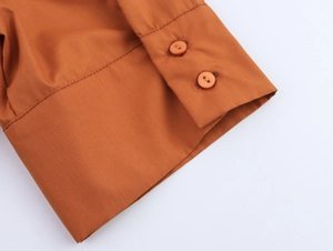 Détail rapproché des poignets à deux boutons d'une robe chemise en popeline rouille