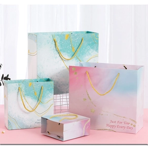 Close-up of pink and teal watercolor paper gift bags with gold handles and starry patterns