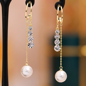 Detail of long gold earrings featuring crystals and elegant white pearls on black stand
