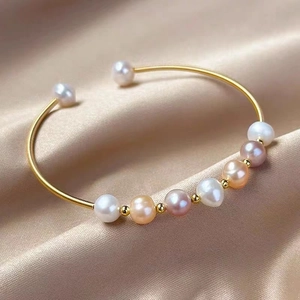 Detail of handmade wire-wrapped gold bracelet with multi-colored pearls on champagne silk
