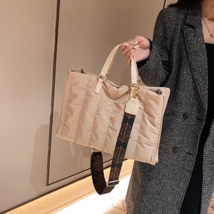 Beige quilted tote bag with vintage patterned strap held by model in neutral setting