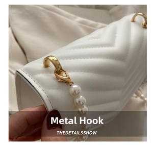 Detail view of gold metal hooks and white pearl strap on V-shaped quilted leather bag