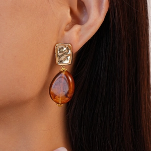 Close-up of square gold textured metal and amber resin teardrop earrings on a model
