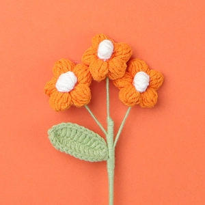 Macro shot of three orange handmade crochet flowers with green leaves on orange paper