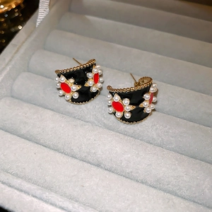 Detailed view of vintage C-shape earrings with black enamel and red pearl floral patterns