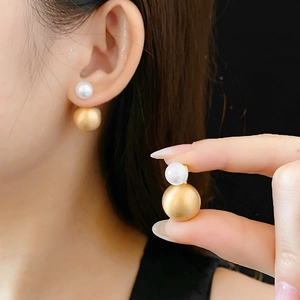 Detail of elegant gold metal and white pearl double-bead earrings on model