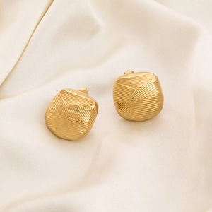 Macro view of gold-plated geometric earrings with cross-brushed texture on silk