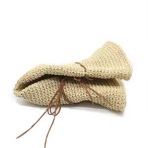 Detail of a foldable beige straw hat showing flexible woven texture and leather strap