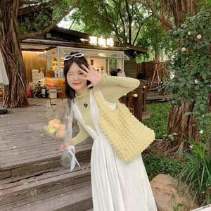 Outdoor shot of a textured yellow puff shoulder bag paired with a white dress and green top