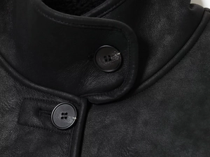 Detail of black faux suede jacket featuring collar texture and metallic buttons