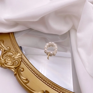 Detail shot of a pearl beaded ring with a gold letter L charm on a vintage mirror