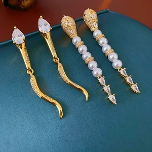 Macro view of gold snake-shaped earrings with pearls and zircon on green leather