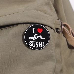 Close-up of a round black metal brooch with I Love Sushi text on a khaki fabric bag