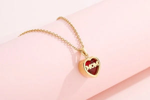 Close-up of gold heart MOM necklace with red birthstone against soft pink background