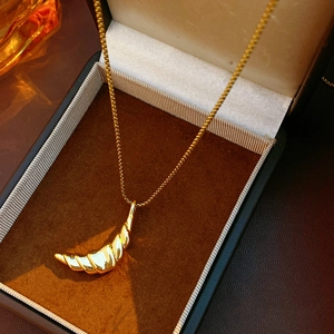 Macro shot of a gold-plated croissant pendant necklace inside a luxury jewelry gift box