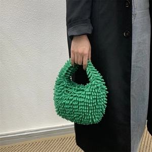 Green plush stripe handbag held by model in black coat for a trendy autumn winter look