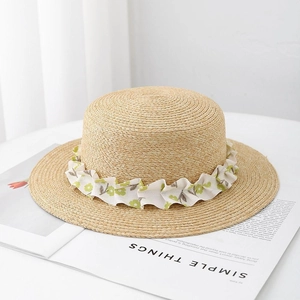 Flat top straw sun hat with green floral ribbon trim on a minimalist lifestyle background