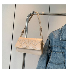 Close-up of beige quilted leather crossbody bag with knot strap detail and flap closure