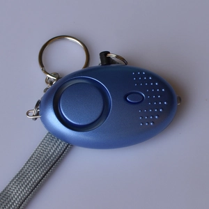 Blue personal alarm for women with metal keychain and grey lanyard on purple surface