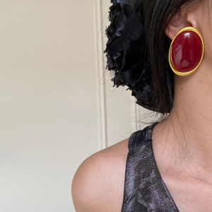 Close-up of retro oval earring with deep red center and matte gold metal frame on model