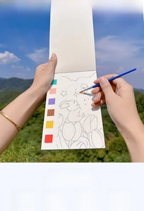 Portable watercolor coloring book with rabbit line art and a blue brush in outdoor nature