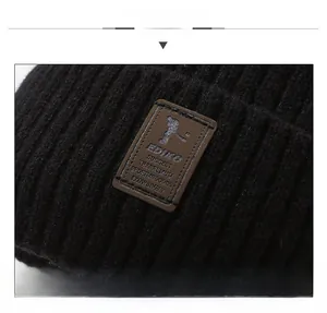Detailed view of the black knit beanie featuring a brown leather logo patch with stitching
