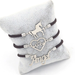 Detail of three braided rope bracelets with unicorn, heartbeat, and Angel pendants on a pillow