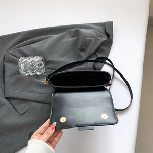 Minimalist black leather crossbody bag with gold magnetic buckle on a grey blazer
