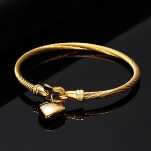 Close-up of golden twisted wire bracelet with polished heart pendant on black surface