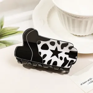 Close-up of cow print hair claw clip with black star detail on a cream surface