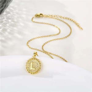 Close-up of golden round pendant with letter L engraving and delicate beaded border edge