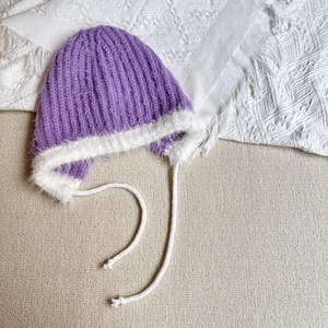 Close-up of purple knit hat with plush white trim and twisted tie straps for winter