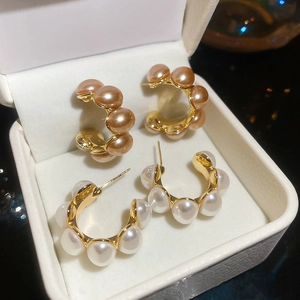 Detailed macro of C-shaped champagne and white pearl earrings in gold plated finish