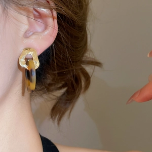 Close-up of golden geometric earrings with tortoise shell resin pendants on a model