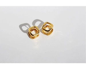 Detail of hollow square gold-plated earrings with sharp geometric shadows on white background